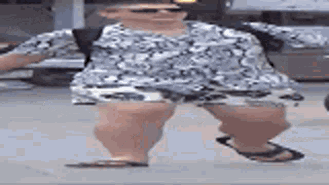 a man in a floral shirt and shorts is standing on a sidewalk wearing flip flops .