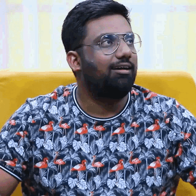 a man wearing glasses and a flamingo shirt is sitting on a yellow couch