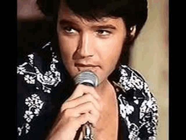 elvis presley is singing into a microphone in a close up of his face .