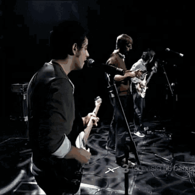 a man singing into a microphone while playing a guitar in a band