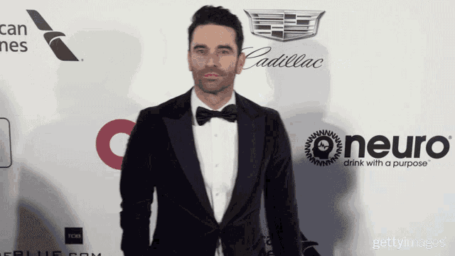 a man in a tuxedo is standing on a red carpet with a neuro logo in the background