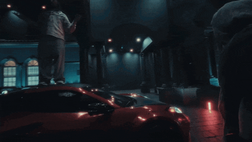 a man stands on top of a red car in a dark building