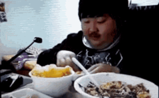 a man is sitting at a table with bowls of food and a microphone .