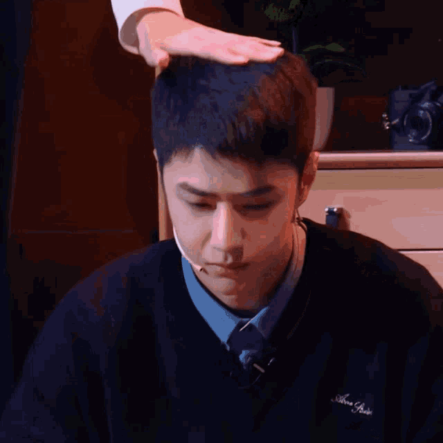 a man 's head is being touched by another person while wearing a black sweater with the word abercrombie on the front
