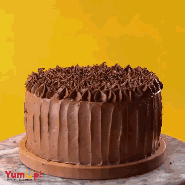 a chocolate cake is sitting on a table with a yellow background and the words yum up on the bottom