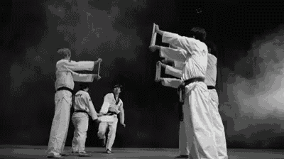 a black and white photo of a group of karate fighters performing a trick on a stage .