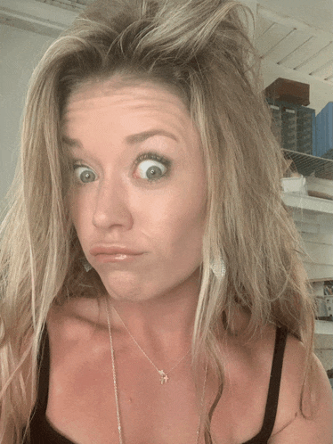a woman wearing a black tank top and a necklace makes a funny face