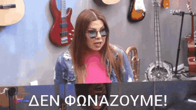 a woman wearing sunglasses is sitting in front of a wall with guitars and the words den fonazoume