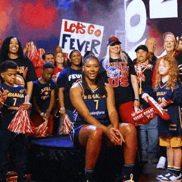 a woman sitting in front of a sign that says " let 's go fever "