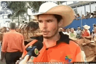 a man wearing a cowboy hat is holding a microphone in front of a crowd