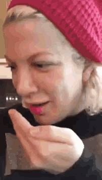 a woman wearing a pink hat is blowing a kiss with her hand