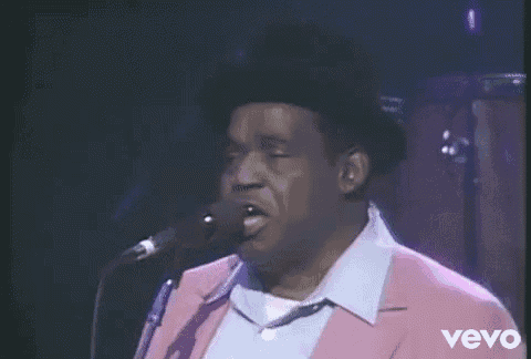 a man is singing into a microphone while wearing a pink jacket .