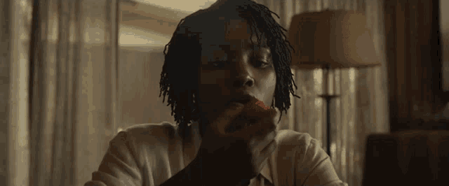a woman with dreadlocks is eating a strawberry while sitting at a table in a living room .
