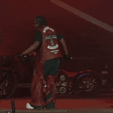 a man wearing sunglasses and a red leather vest is dancing in a dark room .