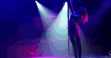 a woman is dancing on a pole on a stage in front of a blue and purple light .