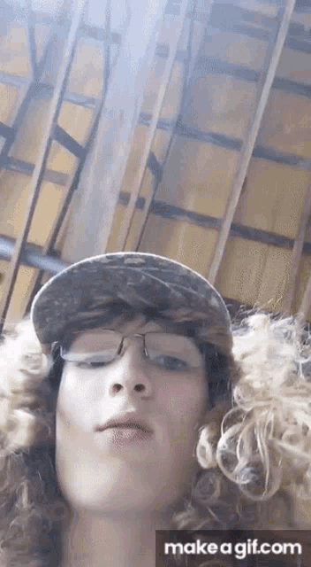 a man with curly hair wearing glasses and a hat is making a funny face