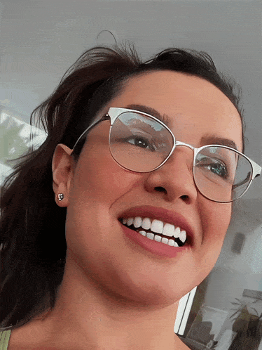 a woman wearing glasses and earrings smiles with her mouth open
