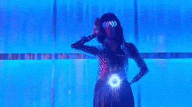 a woman in a sequined dress is standing in front of a blue wall holding a microphone .