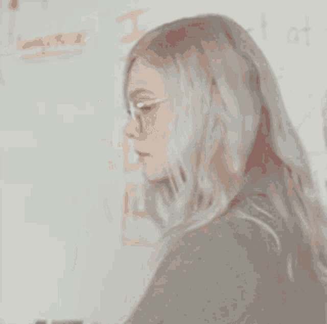 a woman wearing glasses is standing in front of a white board with the word i on it .