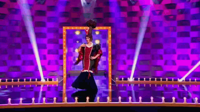 a woman in a red dress is standing on a stage in front of a checkered wall .