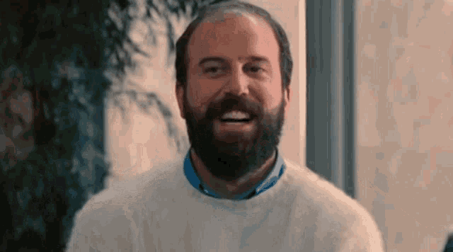a bald man with a beard wearing a white sweater is smiling .