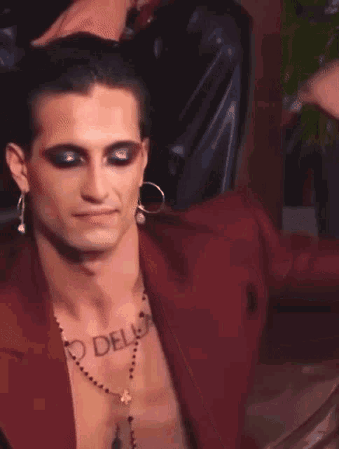 a man with a tattoo on his chest is wearing a red suit and earrings .