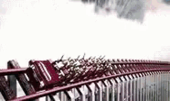 a roller coaster is going over a bridge with a cloudy sky in the background .