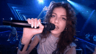 a woman is singing into a microphone with a blue background