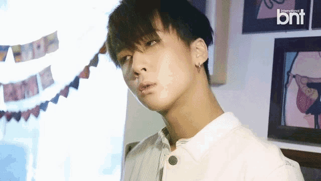 a young man wearing a white shirt and earrings is standing in front of a wall with pictures .