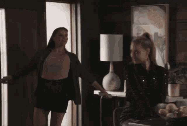 two women are standing in a room with a lamp