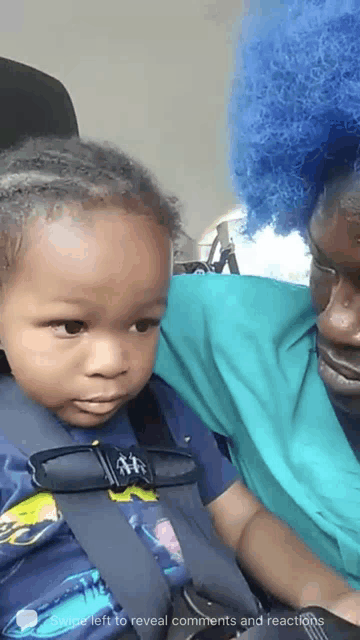 a woman with blue hair is holding a child in a car seat