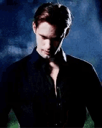 a shirtless man in a black shirt is standing in the dark .