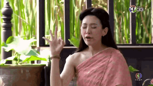 a woman in a pink dress is sitting in front of a balcony with her eyes closed and making a funny face .