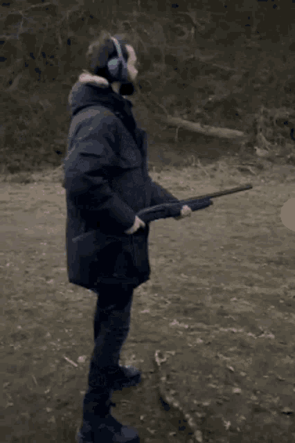 a man with a beard is holding a shotgun and wearing ear muffs