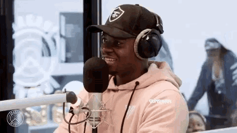 a man wearing headphones and a hat is talking into a microphone in a studio .