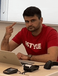 a man wearing a red t-shirt that says istyle is sitting at a desk with a laptop