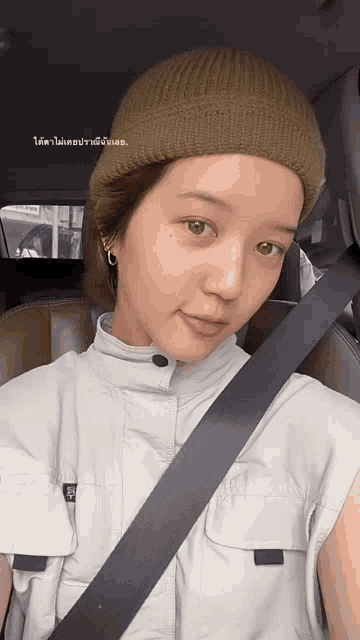 a woman wearing a beanie is sitting in a car with a seat belt .