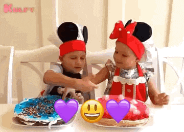 two little girls are sitting at a table with plates of food . one of the girls is wearing a mickey mouse hat .