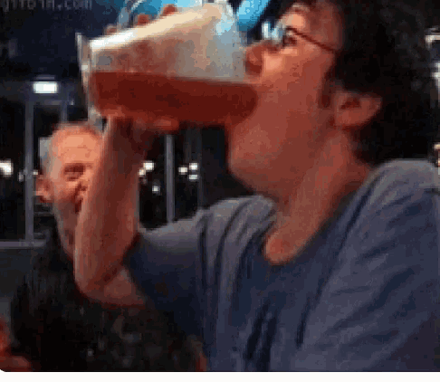 a man is drinking a large glass of red liquid from a plastic cup