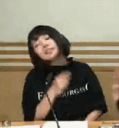 a woman in a black shirt is sitting at a table holding a microphone .