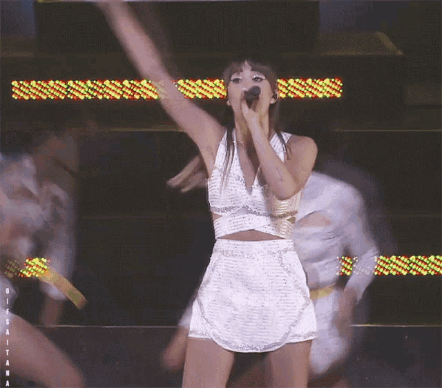 a woman in a white dress is singing into a microphone on a stage