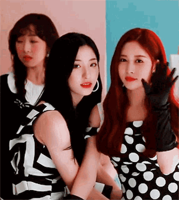 three women are posing for a picture together and one of them is wearing a black and white polka dot dress .