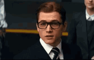 a man wearing glasses and a suit and tie is sitting in a classroom .