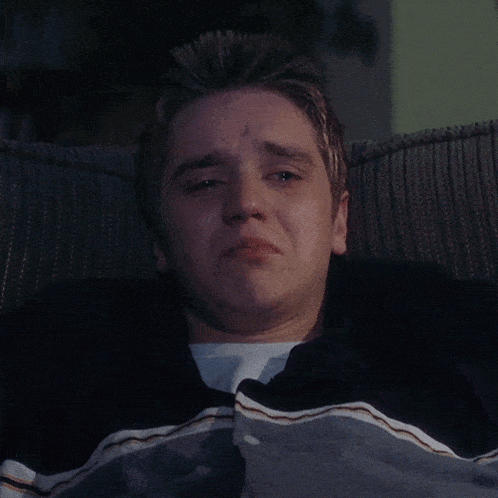 a young man is crying while laying on a couch with a blanket