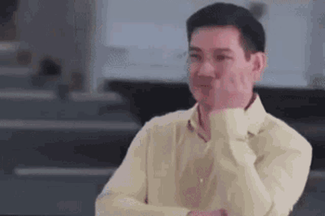 a man in a yellow shirt is making a funny face with his hand .