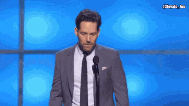 a man in a suit and tie stands in front of a microphone with the hashtag @royals_jm on the bottom