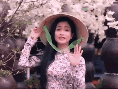 a woman wearing a conical hat and a floral dress is waving her hand .