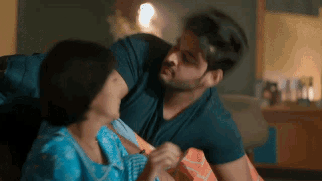 a man and a woman are sitting on a bed and the man is holding the woman 's neck .