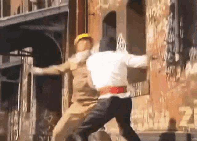 a man in a white shirt is fighting another man in a yellow hat .