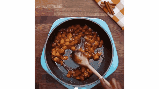 a person is cooking food in a pan with a wooden spoon .